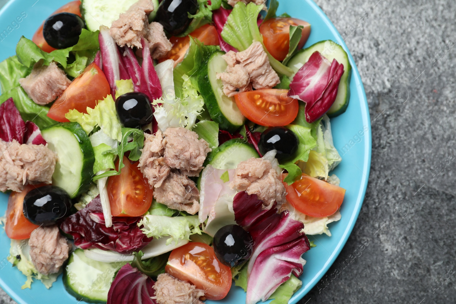 Photo of Plate of delicious salad with canned tuna and vegetables on grey table, top view