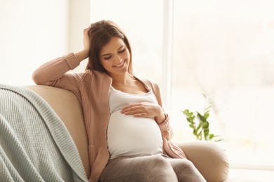 Photo of Young pregnant woman sitting on couch in living room