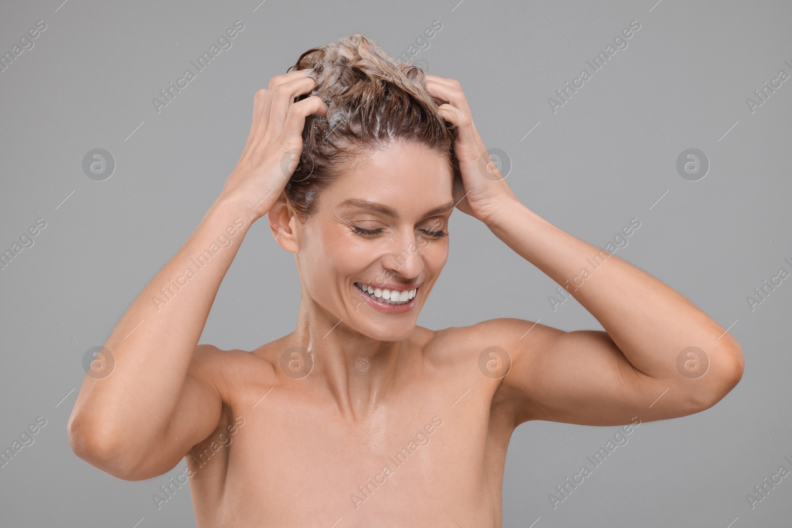 Photo of Beautiful happy woman washing hair on light grey background