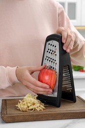 Woman grating fresh red apple at kitchen table, closeup