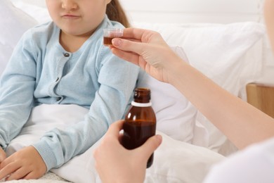 Mother giving cough syrup to her daughter in bedroom, closeup