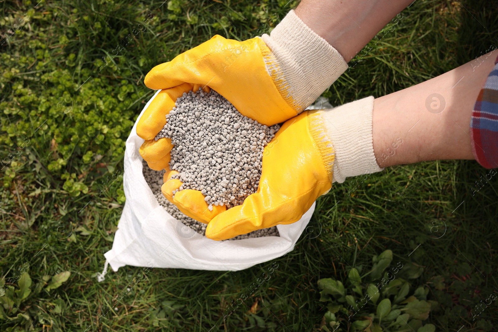 Photo of Woman with fertilizer on green grass outdoors, top view