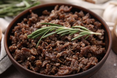 Fried ground meat in bowl and rosemary on table, closeup