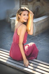 Photo of Beautiful young woman in stylish pink dress sitting on bench outdoors