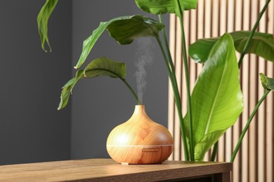 Photo of Air humidifier on wooden table near green houseplant indoors