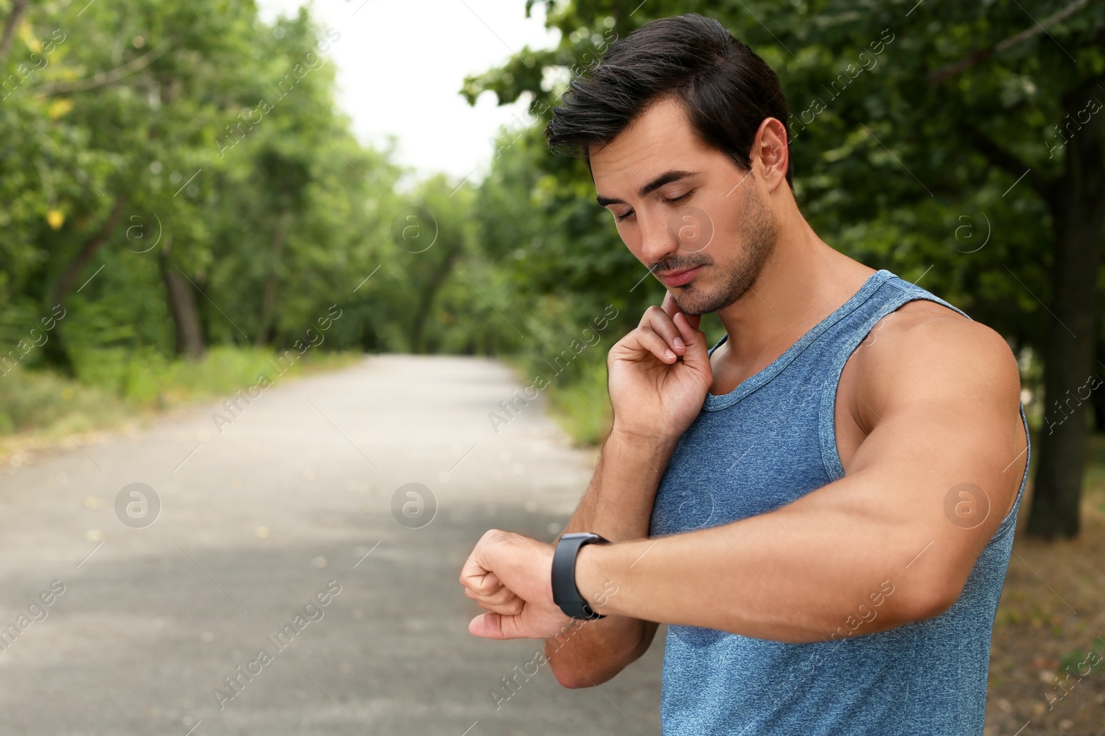 Photo of Young man checking pulse after training in park. Space for text