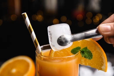 Bartender putting ice cube into glass with Tequila Sunrise cocktail, closeup