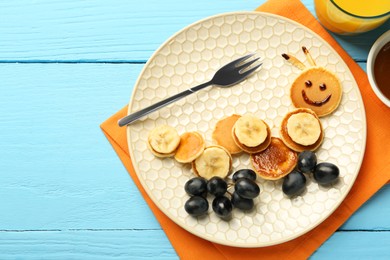 Photo of Creative serving for kids. Plate with cute caterpillar made of pancakes, grapes and banana on light blue wooden table, flat lay. Space for text