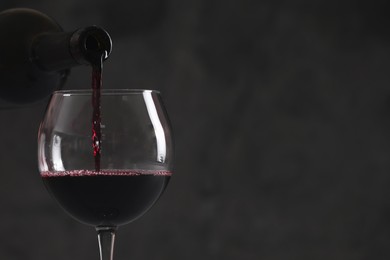Photo of Pouring red wine from bottle into glass on dark background, closeup. Space for text