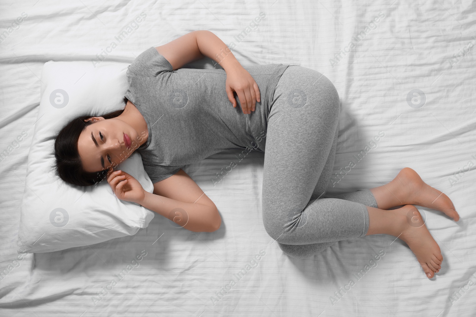 Photo of Young woman suffering from insomnia on bed, top view