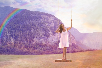 Dream world. Young woman on swing against mountains under sunset sky