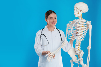 Photo of Female orthopedist with human skeleton model on blue background