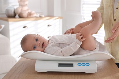 Photo of Young woman weighting her cute baby at home, closeup. Health care