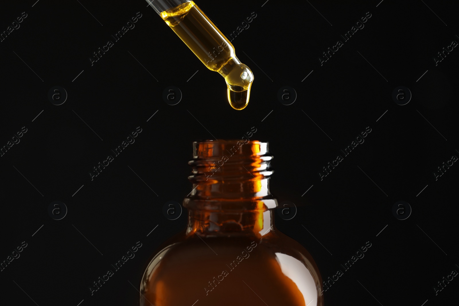 Photo of Pipette with oil over bottle on black background