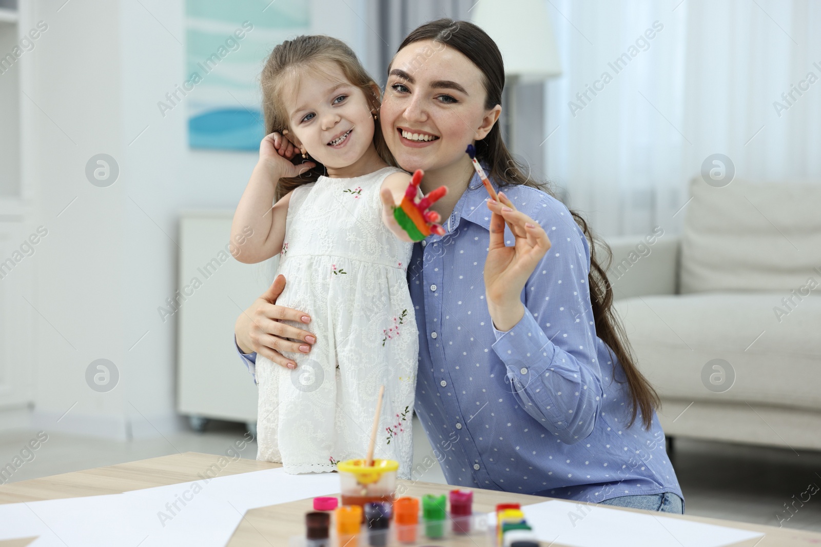 Photo of Mother and her little daughter painting with palms at home