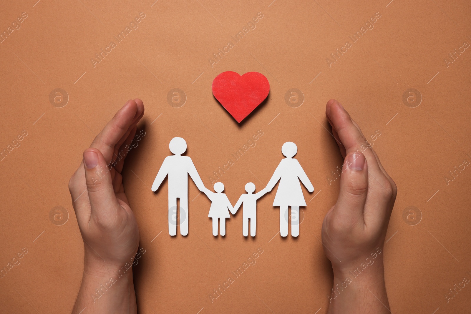 Photo of Man protecting paper family figures and red heart on brown background, top view. Insurance concept