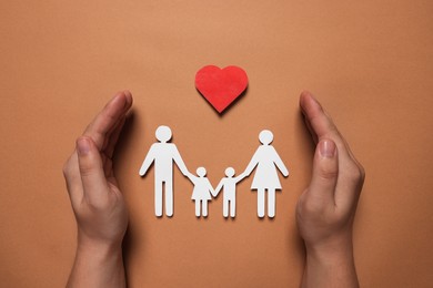 Photo of Man protecting paper family figures and red heart on brown background, top view. Insurance concept