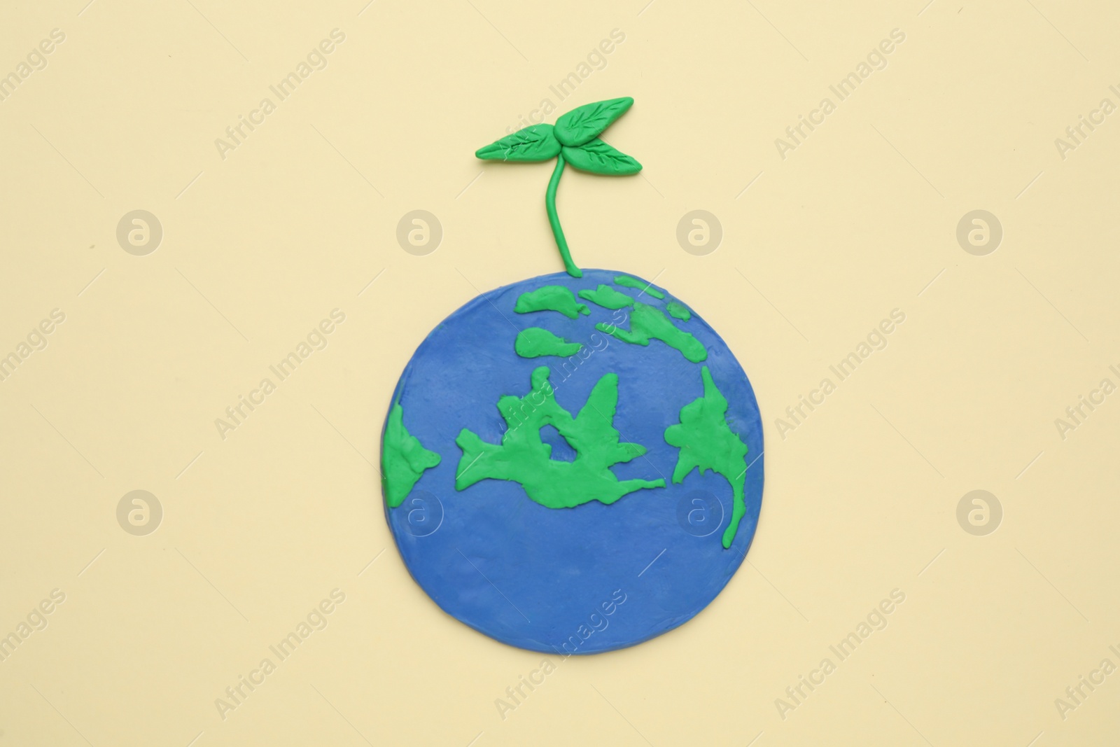 Photo of Plasticine model of planet with green seedling on beige background, top view. Earth Day