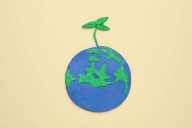 Photo of Plasticine model of planet with green seedling on beige background, top view. Earth Day
