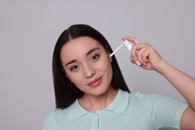 Photo of Young woman using ear spray on light grey background