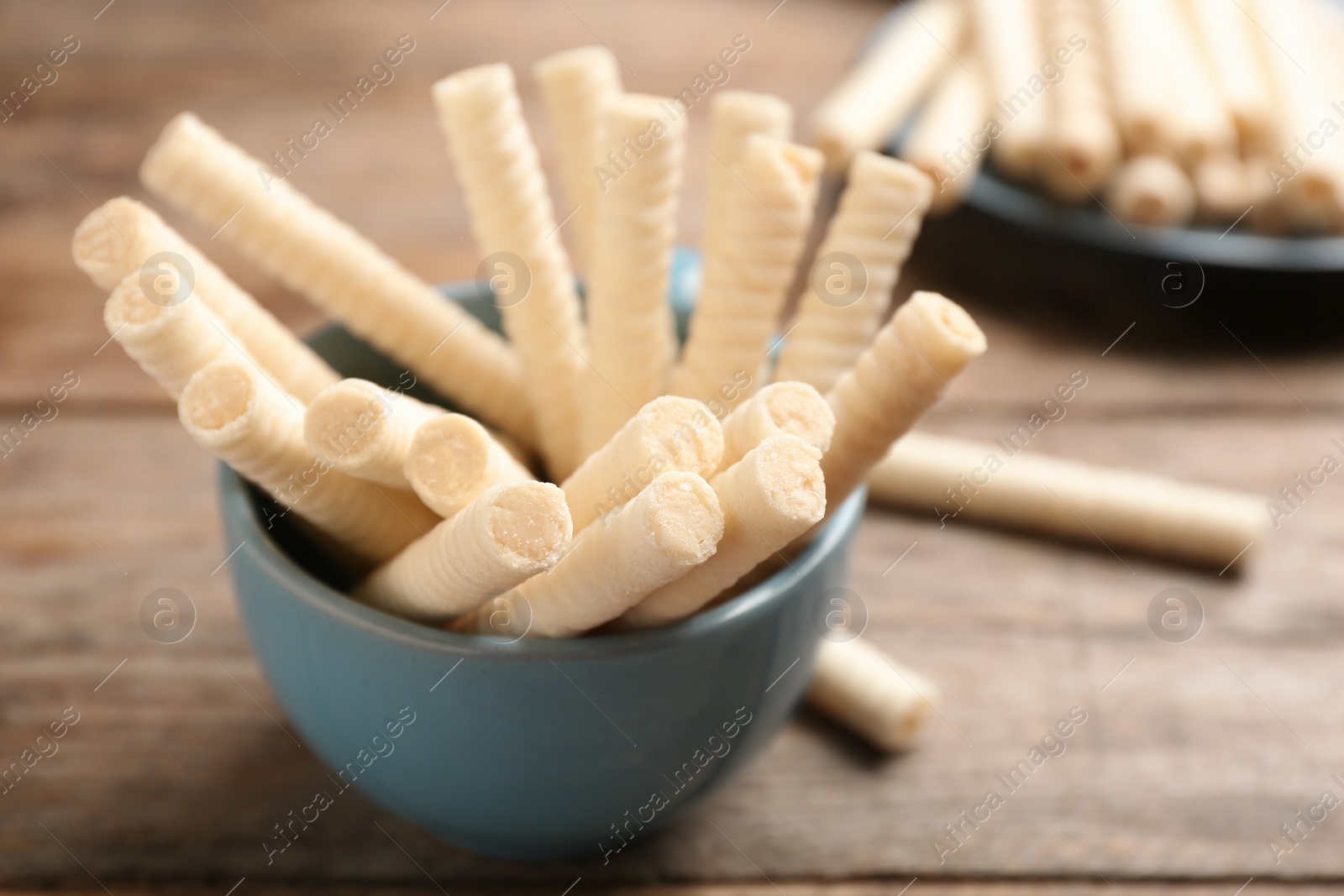 Photo of Bowl with delicious wafer rolls on wooden table, closeup. Sweet food