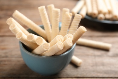 Bowl with delicious wafer rolls on wooden table, closeup. Sweet food