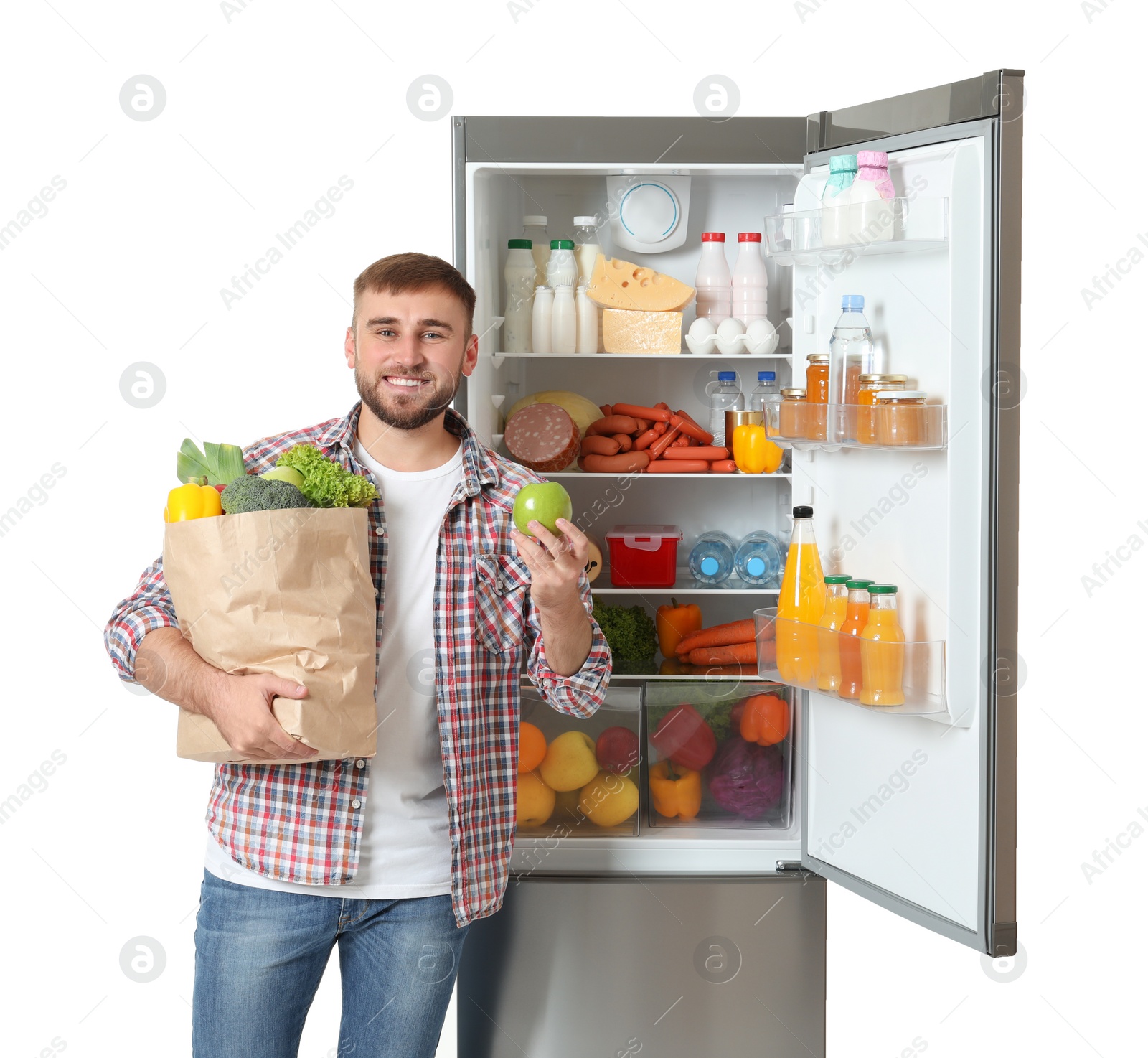 Photo of Young man with bag of groceries and apple near open refrigerator on white background