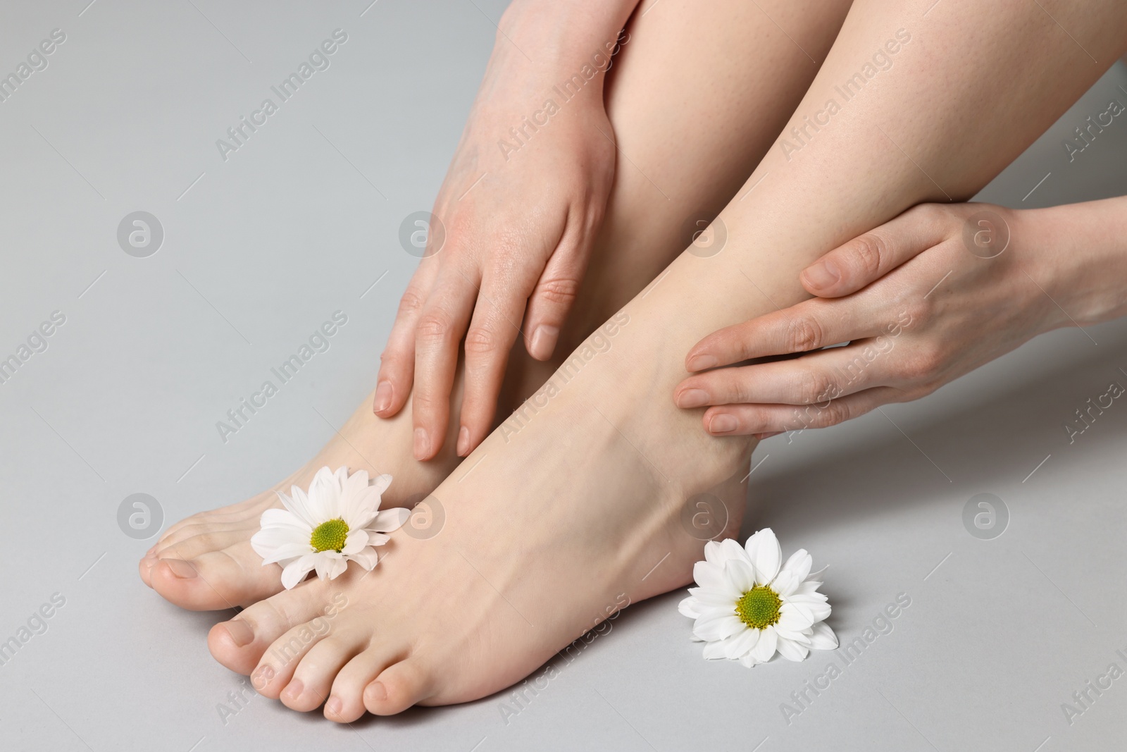 Photo of Closeup view of woman`s groomed feet after care procedure and beautiful flowers on grey background