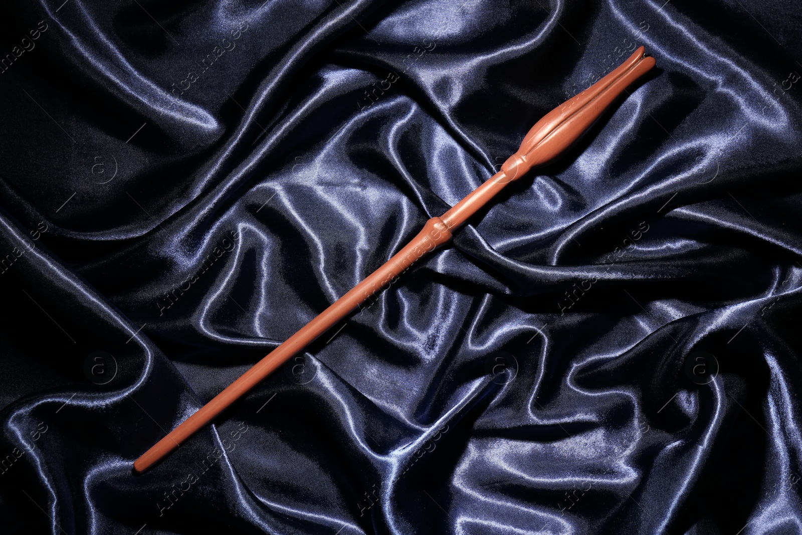 Photo of Old magic wand on dark blue silk, top view