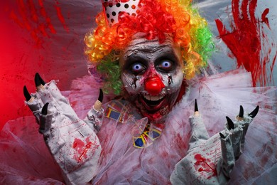 Photo of Terrifying clown near bloodstained plastic film. Halloween party costume