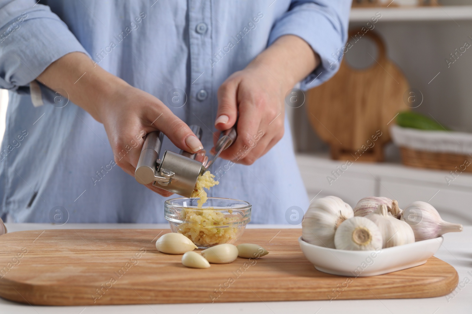 Photo of Woman squeezing garlic with press at white table in kitchen, closeup