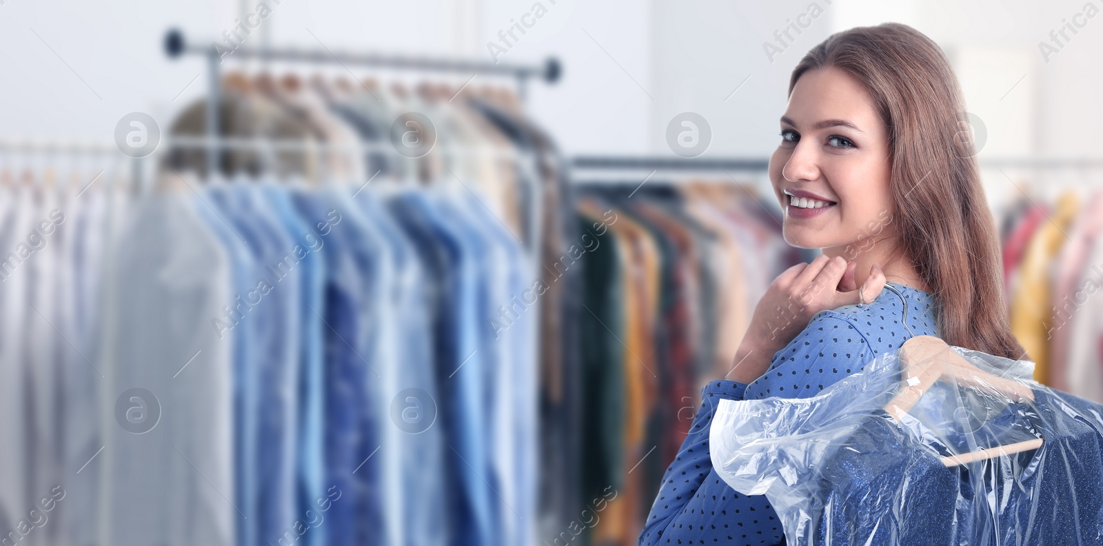 Image of Dry-cleaning service. Happy woman holding hanger with dress in plastic bag indoors, space for text. Banner design