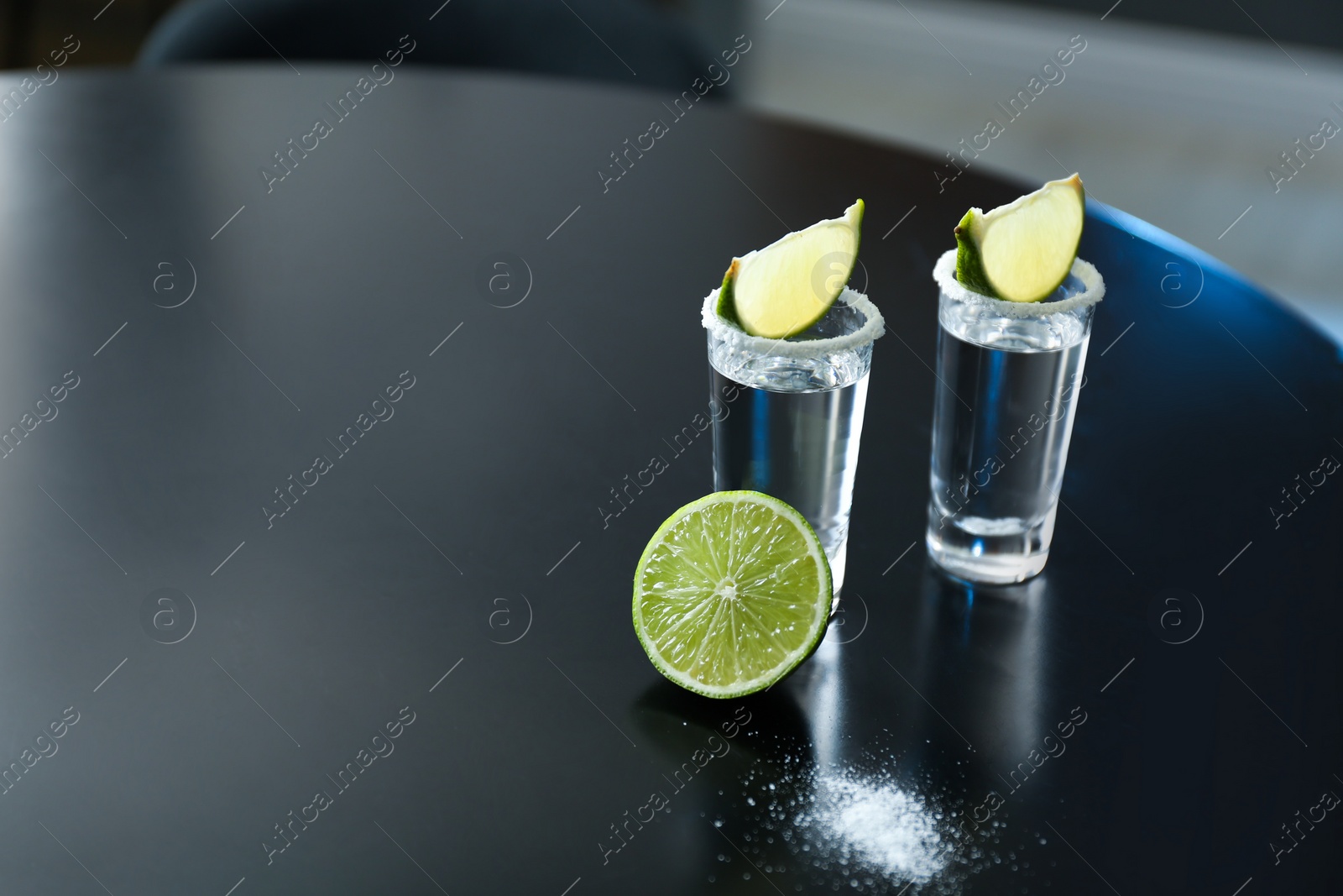 Photo of Mexican Tequila with salt and lime slices on black table at bar. Space for text