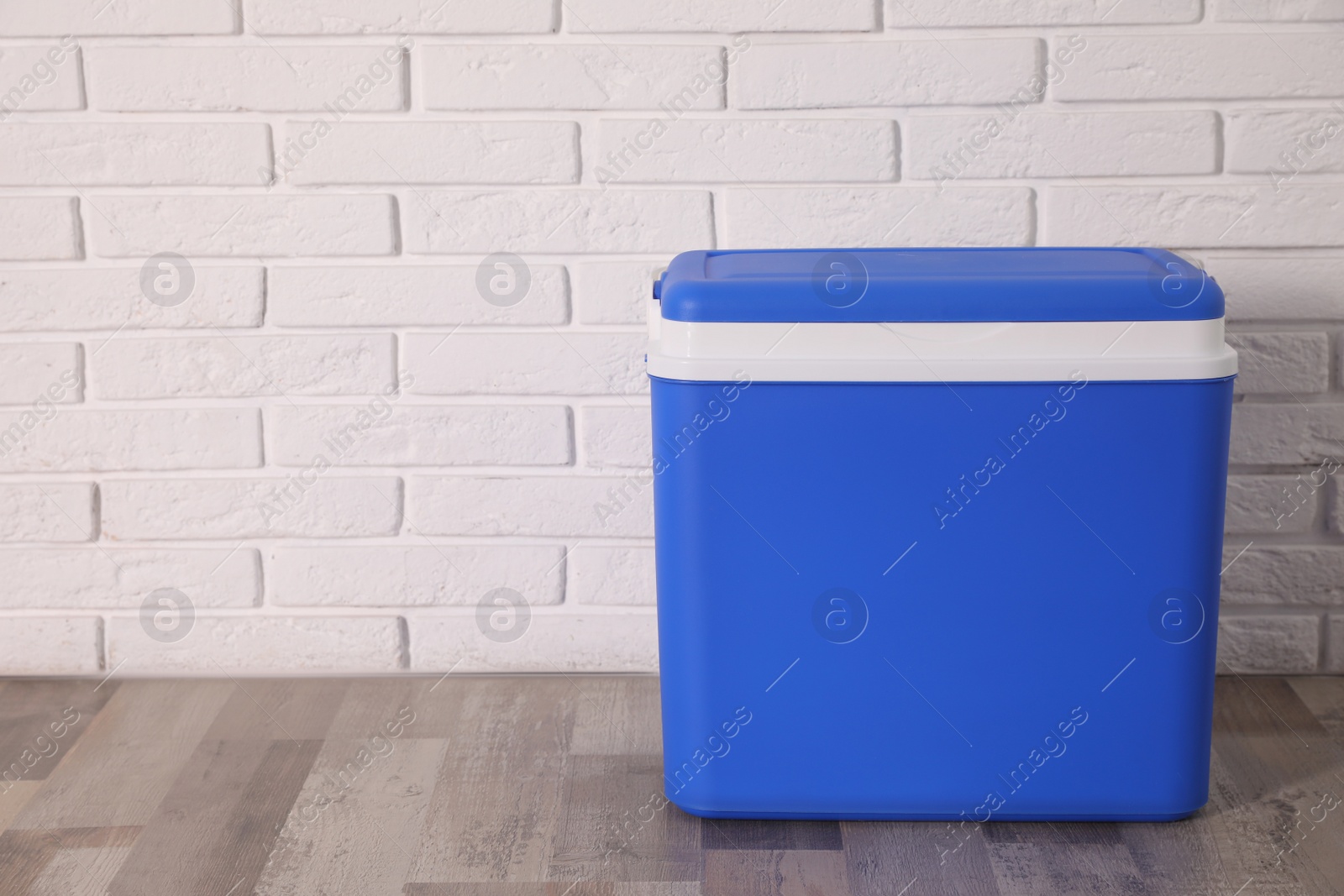 Photo of Closed blue plastic cool box near white brick wall. Space for text