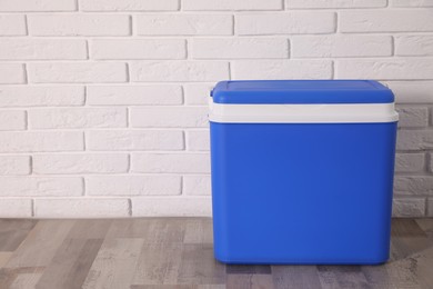 Photo of Closed blue plastic cool box near white brick wall. Space for text