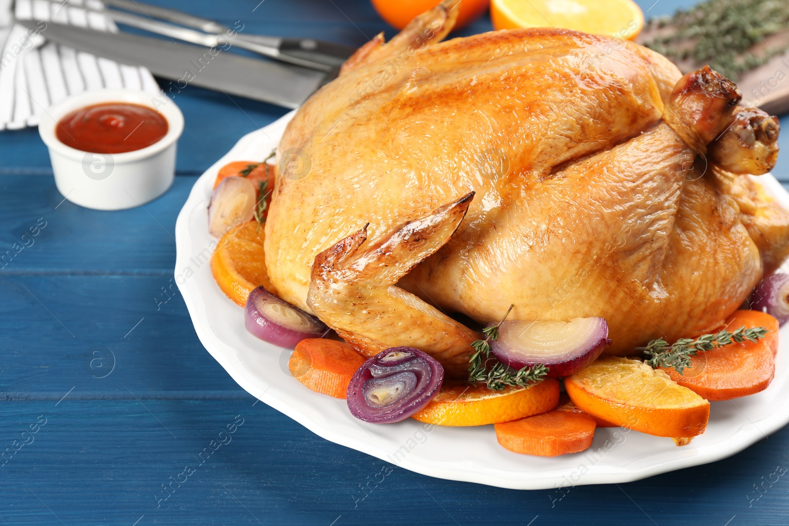 Photo of Roasted chicken with oranges on blue wooden table, closeup