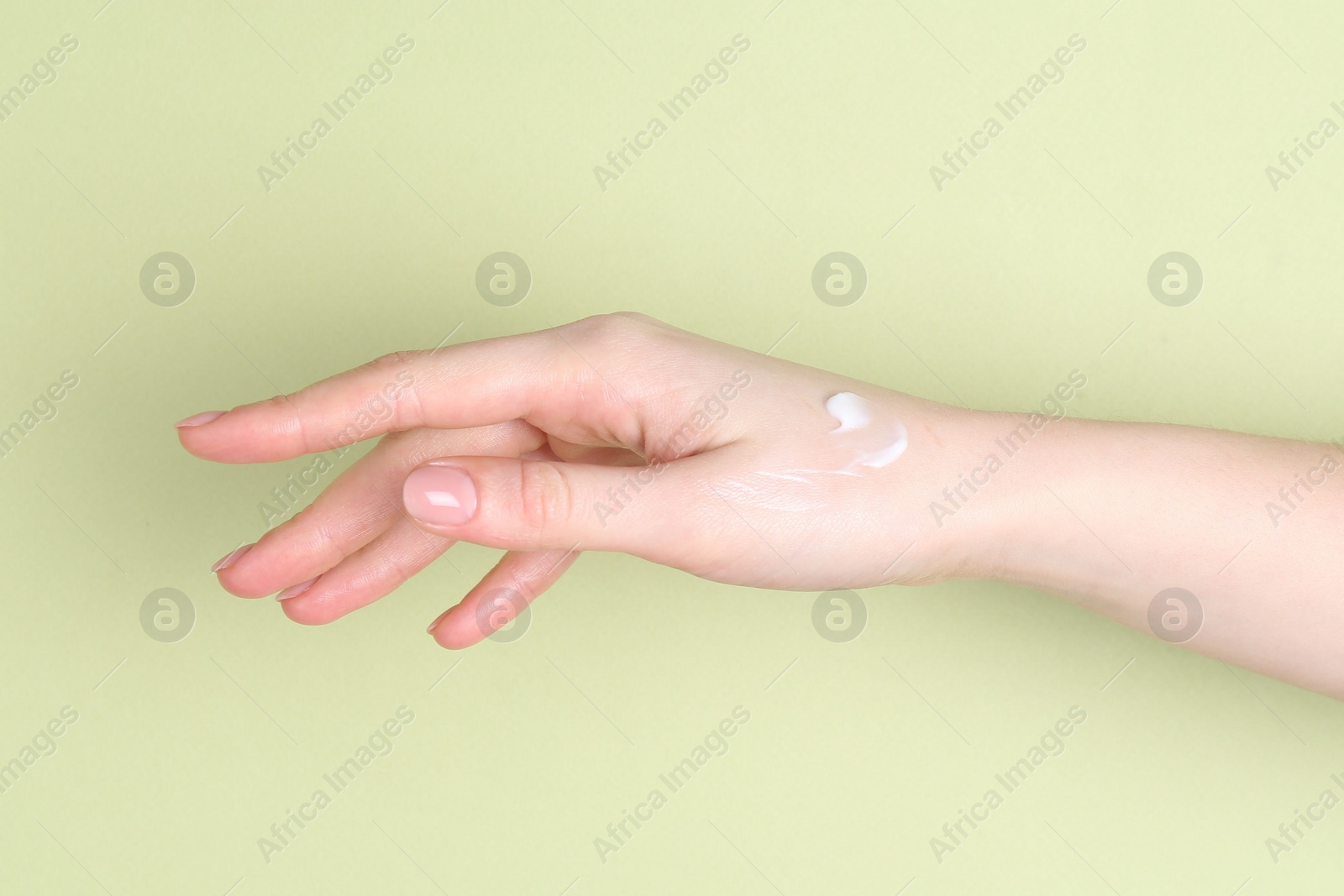 Photo of Woman with cream on her hand against green background, closeup