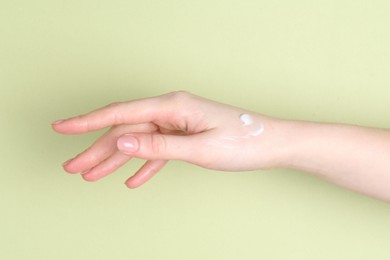 Woman with cream on her hand against green background, closeup