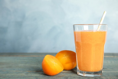 Photo of Tasty persimmon smoothie with straw and fresh fruit on wooden table against light blue background. Space for text