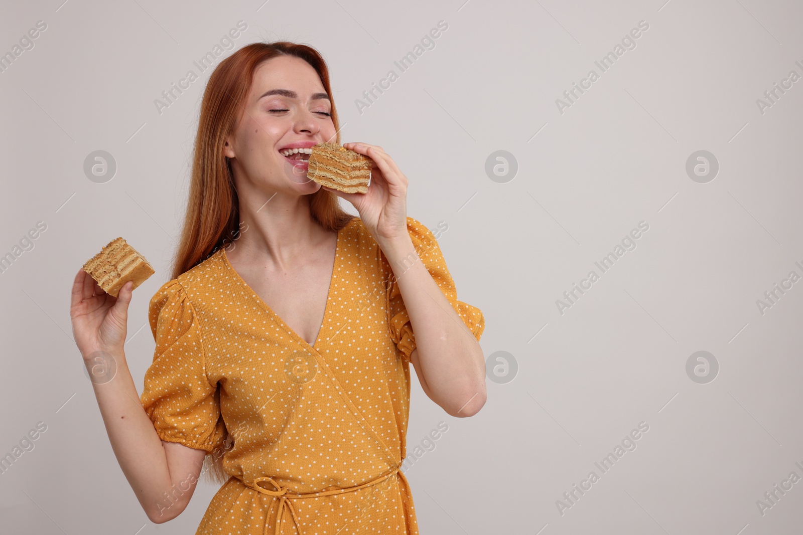 Photo of Young woman eating pieces of tasty cake on light grey background, space for text