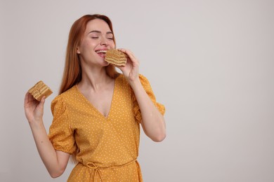 Photo of Young woman eating pieces of tasty cake on light grey background, space for text