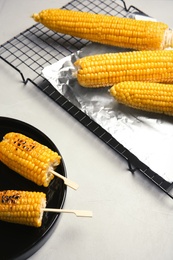 Ceramic plate with grilled corn cobs on light background