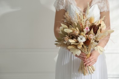 Photo of Bride holding beautiful dried flower bouquet at home, closeup. Space for text
