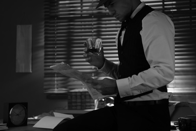 Old fashioned detective with drink and documents in office. Black and white effect
