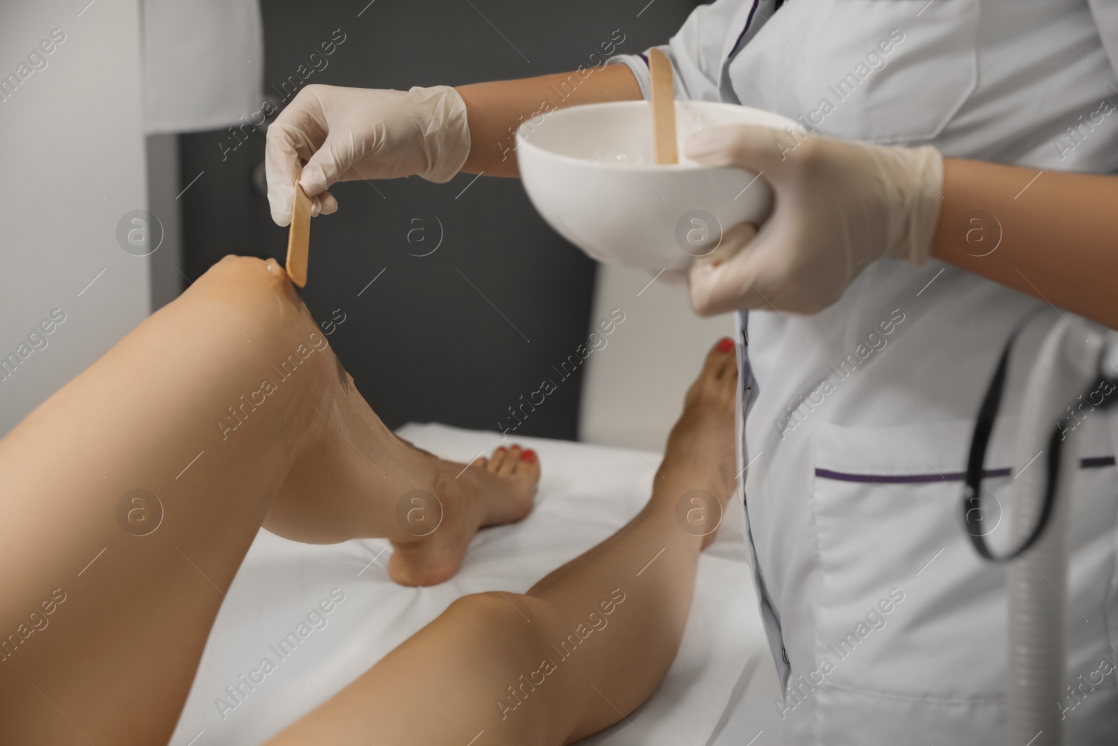 Photo of Professional cosmetologist applying gel on client's leg before laser epilation procedure in salon, closeup