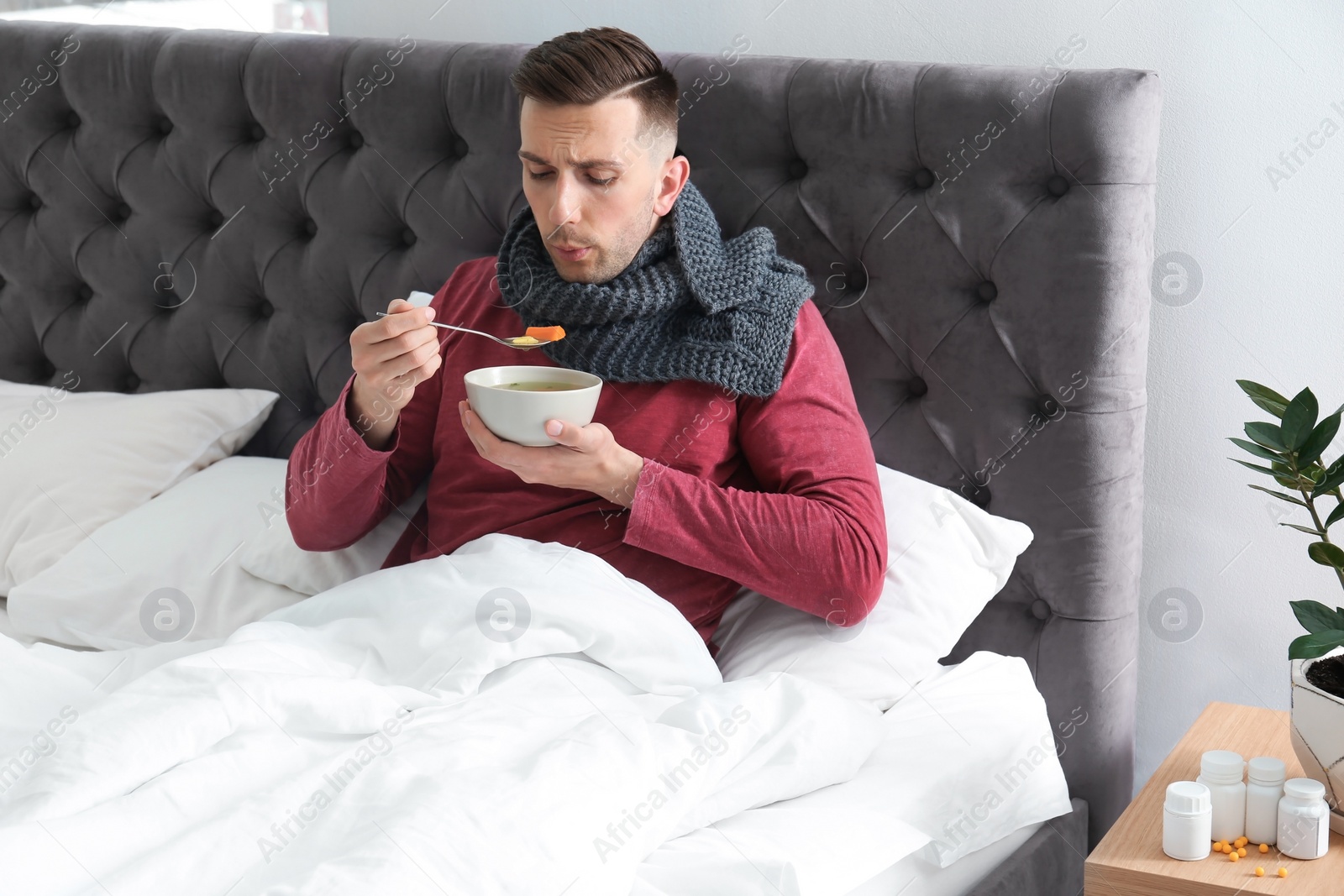 Photo of Sick young man eating broth to cure cold in bed at home