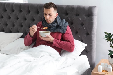 Photo of Sick young man eating broth to cure cold in bed at home