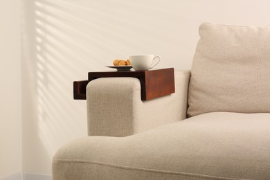 Photo of Cup of coffee and nut shaped cookies on sofa with wooden armrest table indoors. Interior element