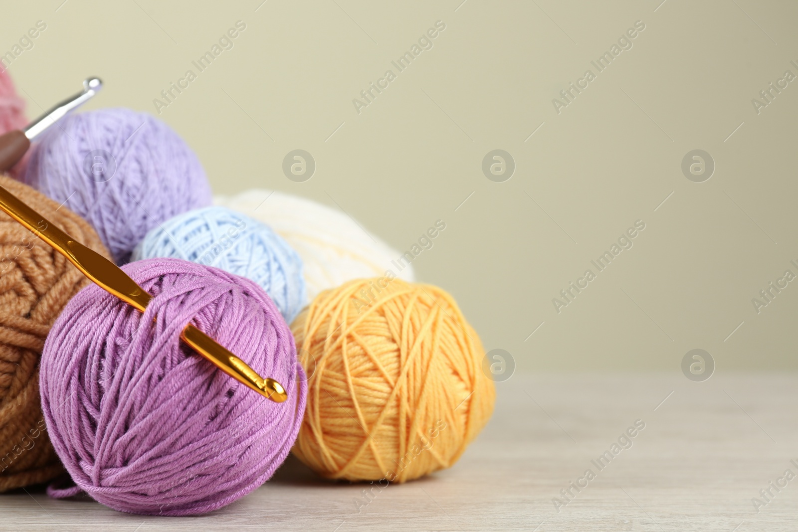 Photo of Clews of colorful knitting threads and crochet hooks on white wooden table against beige background. Space for text