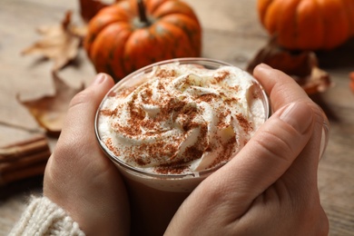 Photo of Woman holding tasty pumpkin latte at table, closeup